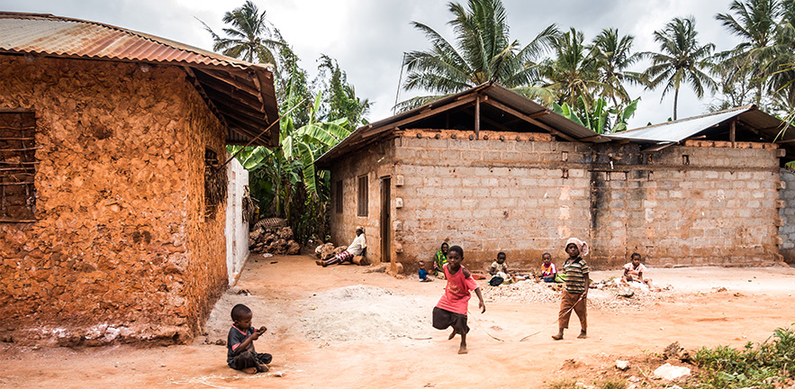 Zanzibar, Tanzania - September 16, 2015: Young kids playing in front of their houses in Kilimani village (Zanzibar). One house is made out of bricks and the other one from the stone. Father and mother are sitting in front of the house and watching kids.