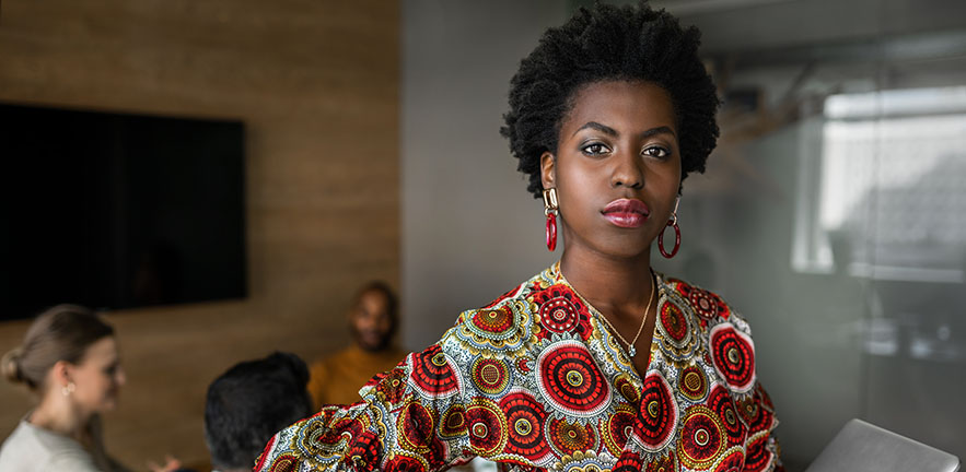 Beautiful young confident professional black african business woman holding laptop, coworkers hold a meeting in background.